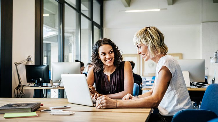 Two woman smiling while working on laptop	