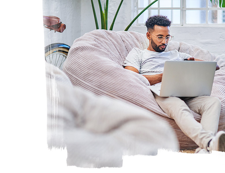 Man sat on cushion, working on his laptop.