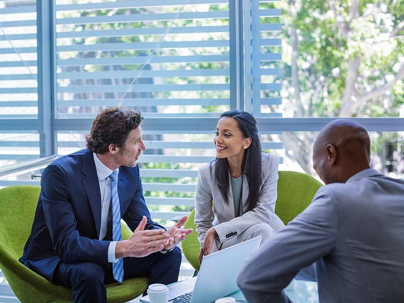 Three people gathered having a discussion, sat on green chairs.