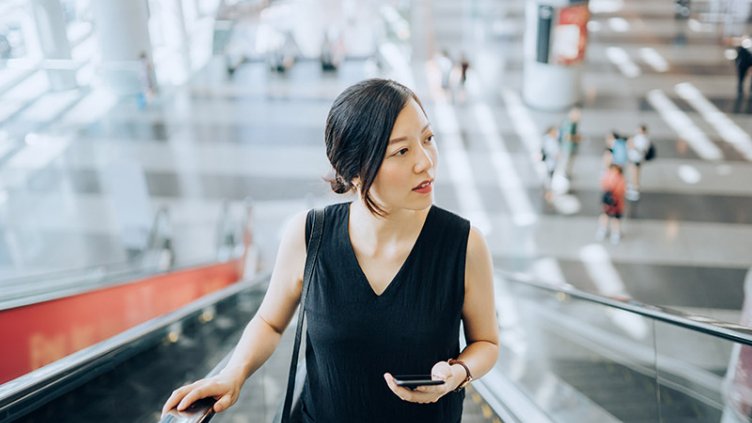 A girl holding mobile and going on escalator