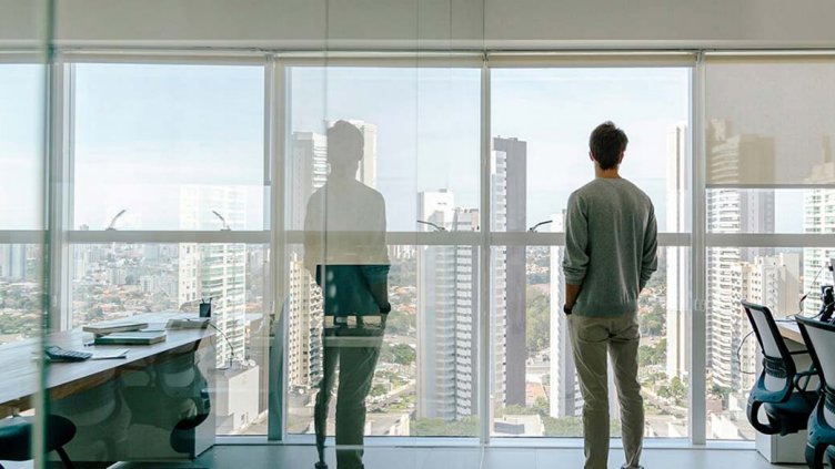 young man looks out of office window over city